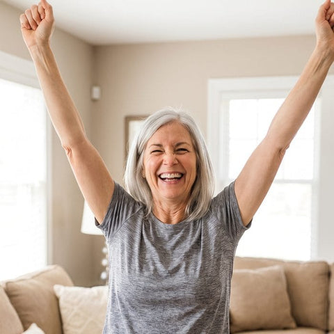 A woman at home cheering with both arms raised