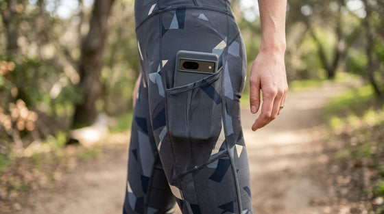 Close-up of a smartphone tucked into the side pocket of a patterned activewear legging being worn outdoors