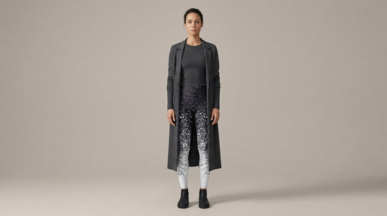 Woman standing full length in a charcoal monochrome column outfit with black-to-white ombre FIERCEPULSE leggings and a long open duster coat