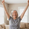A woman at home cheering with both arms raised